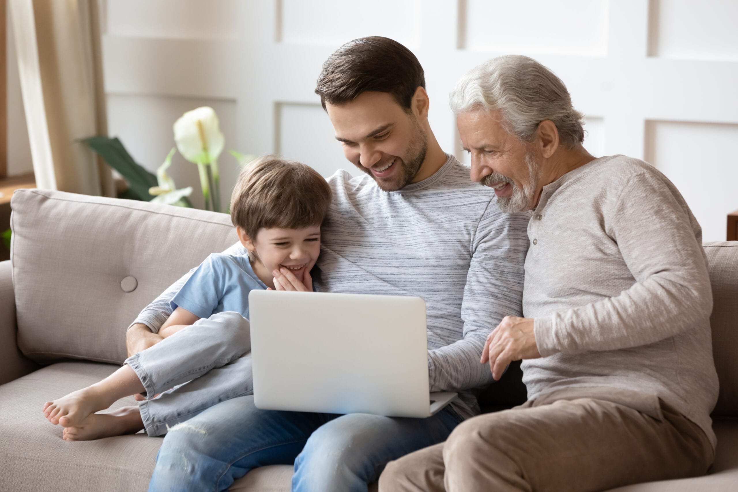 Happy little boy with father and grandfather using laptop together